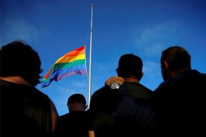 Mourners gather under an LGBT pride flag flying at half-mast for a candlelight vigil in remembrance for mass shooting victims in Orlando, from San Diego, California, U.S. June 12, 2016.  REUTERS/Mike Blake - RTX2FVBC